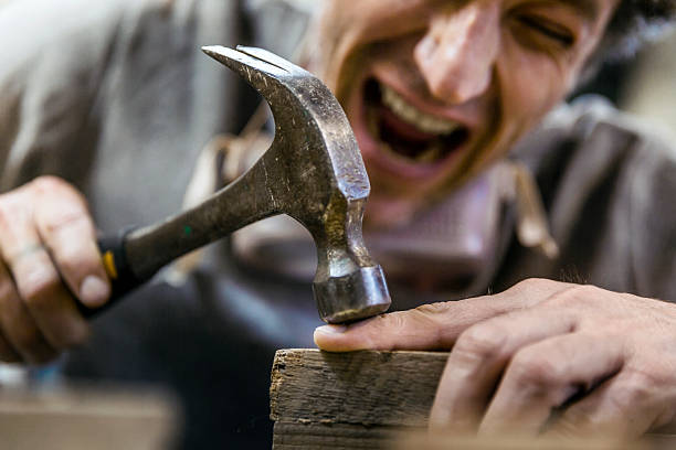 A photo of carpenter accidentally hit his finger with hammer. Mature craftsperson is crying in pain. He is screaming in workshop.