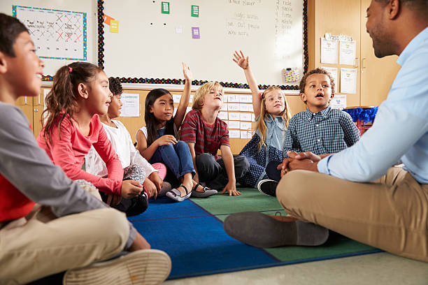 istock Elementary school kids and teacher sit cross legged on floor 515274968