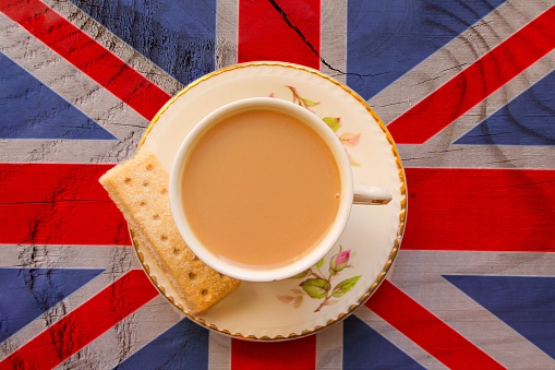 The Union Jack flag with a cup of tea served with a shortbread biscuit in a bone china cup and saucer