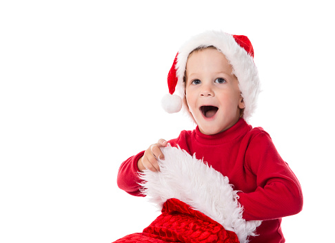 Amazing baby in Christmas hat checking stocking with gifts, isolated on white