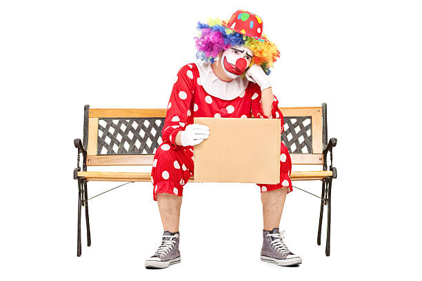 istock Sad clown sitting on bench and holding a sign 515276971