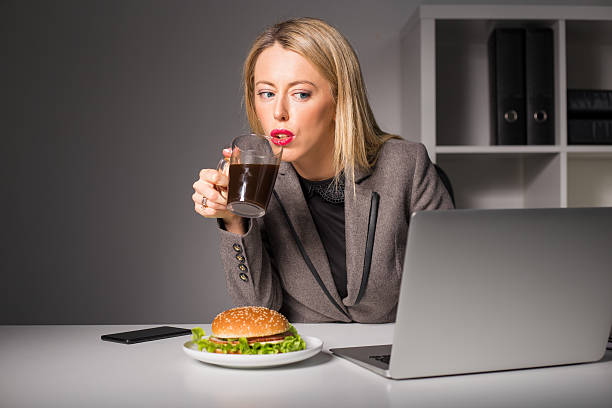 mulher a trabalhar e ter café e hambúrguer para o almoço - eating sandwich emotional stress food imagens e fotografias de stock