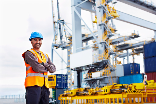 Portrait of a young man in workwear standing outside on a large commercial dock