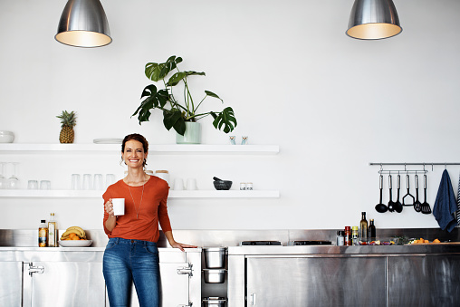 Portrait of a smiling mature woman standing in her kitchen drinking coffee