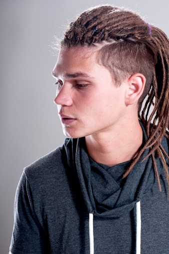Portrait of young stylish guy with dreadlocks collected in bunch on  gray background.