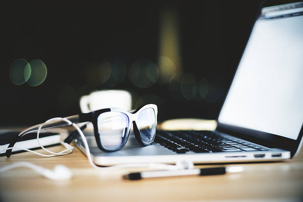 Eyeglasses on opened laptop with blank screen and headphones and pen, mock up