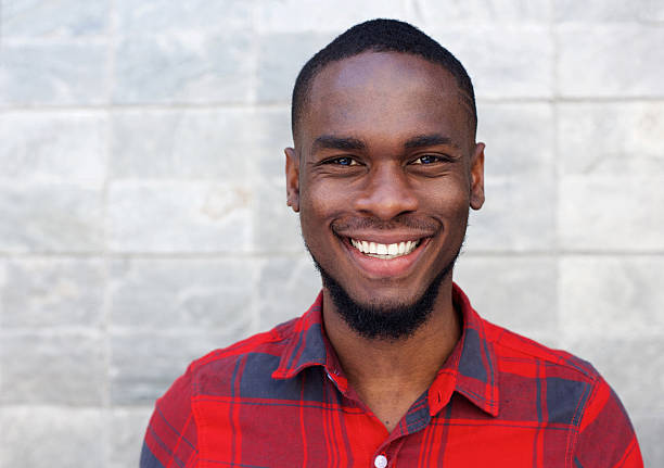 glückliche junge afrikanische mann lächelnd gegen wand grauen - 20 24 jahre fotos stock-fotos und bilder