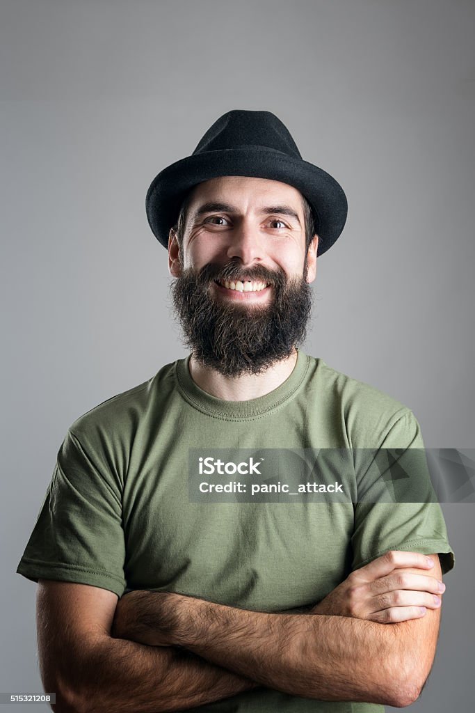 Bearded hipster wearing hat with upper lips piercing friendly laughing Bearded hipster wearing hat with upper lips piercing friendly laughing at camera. Headshot portrait over gray studio background with vignette. Men Stock Photo