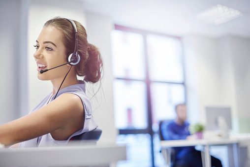 Young smiling trader in headphones talking to customer and discussing financial situation in office