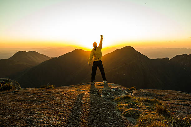 Man celebrating success on top of a mountain Man celebrating success on top of a mountain with one arm Raised and Hands Closed on top of stock pictures, royalty-free photos & images