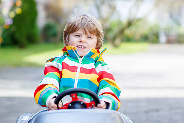 poco niño de conducción en edad preescolar big juguete viejo vintage car, al aire libre - car child teamwork sports race fotografías e imágenes de stock