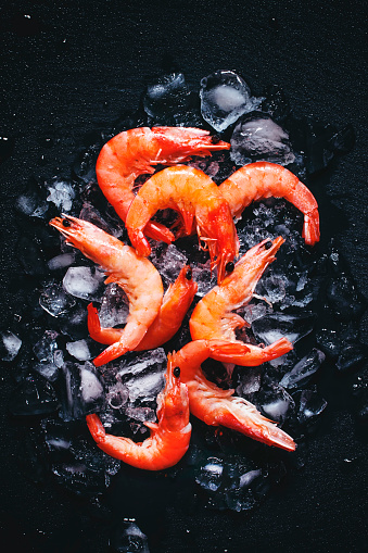 Food background, frozen cooked shrimp with ice, black background, top view