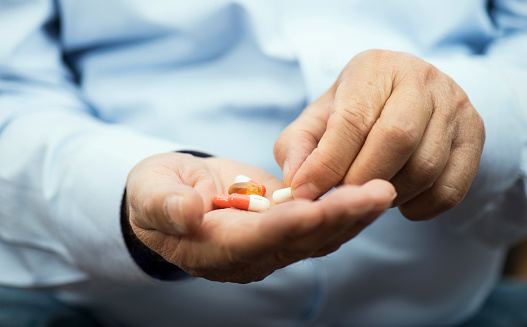 Senior man is holding yellow gel capsules in hand, horizontal