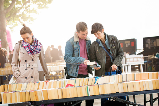 Three young British people shopping for books outdoors at a small London fair.