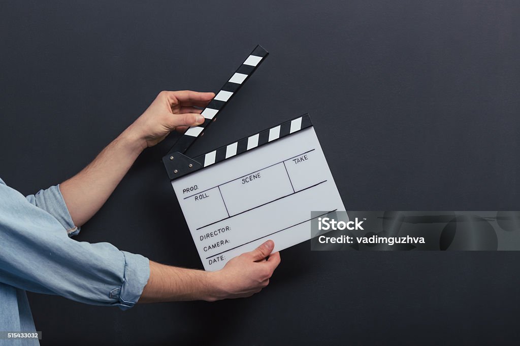 Handsome guy with clapperboard Handsome young man in jeans shirt is holding a clapperboard, standing against blackboard, close-up Film Slate Stock Photo