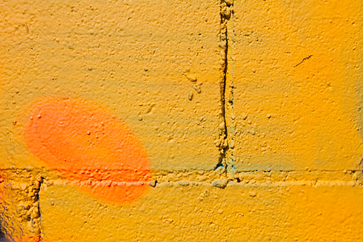 Yellow paint and orange spot on black wall, in a public fence filled with grafittis. Many paint layers on this wall. 