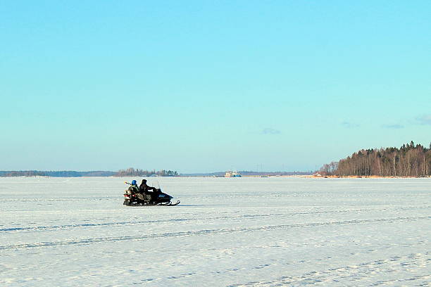 Two men riding on a snowmobile winter Two men riding on a snowmobile winter river. Winter fishing. Snowmobile trailer. The man in the trailer rests.I can not see people's faces. Snowfall. Copy space. Snowmobiling stock pictures, royalty-free photos & images