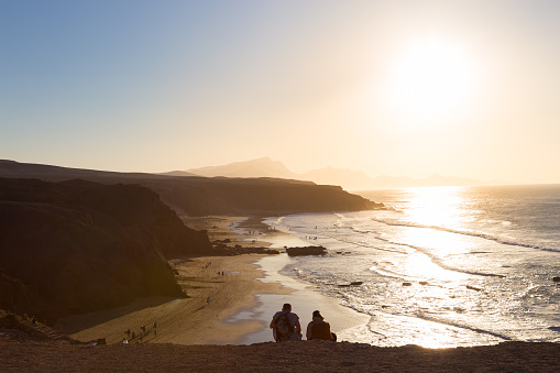 Couple watching surfers riding waves on La Pared beach at sunset, Fuerteventura, Canary Islands, Spain