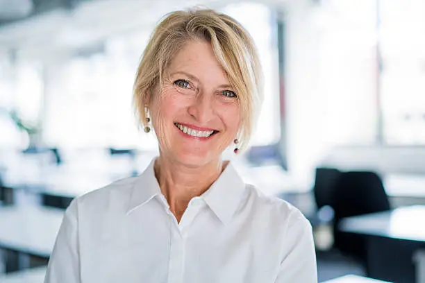 A photo of happy businesswoman in office. Portrait of smiling female professional in formals. Mature executive is at brightly lit workplace.