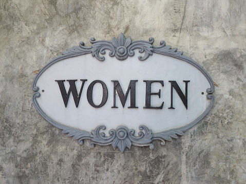Women sign in vintage frame on exposed concrete wall.