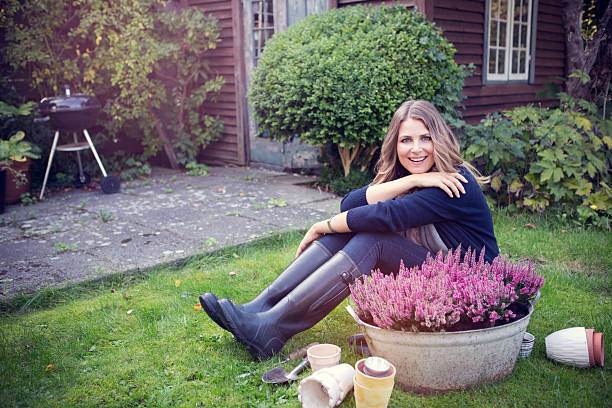 Attractive woman wearing autumn clothes and gum boots planting flowers in garden.