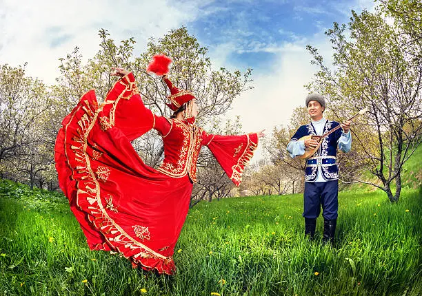 Kazakh woman dancing in red dress and man playing dombra at Spring Blooming garden in Almaty, Kazakhstan, Central Asia