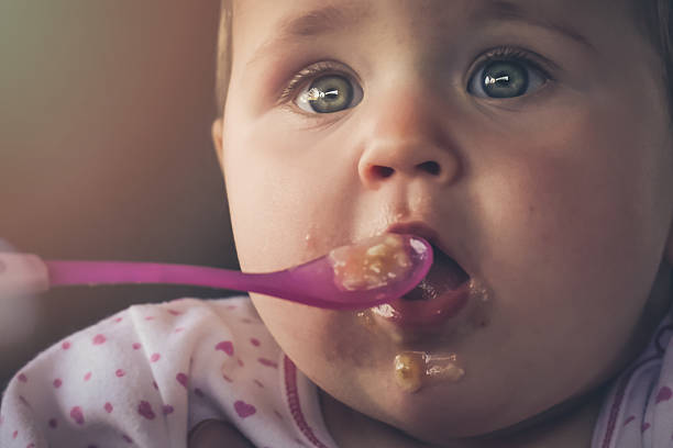istock Feeding a baby girl with a spoon - messy 515477832