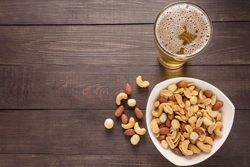 Glass of beer and almond, macadamia, peanut, cashew nut on the wooden background.
