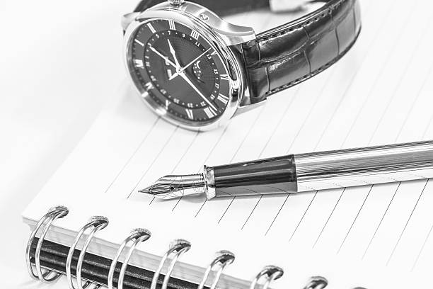 istock Black and white fountain pen on blank notepad and watch 515483312