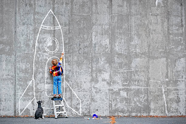 Dream Big Little boy drawing a huge rocket on the wall. dreamlike stock pictures, royalty-free photos & images