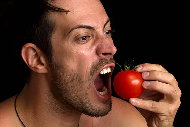 man biting a tomato isolated over black background