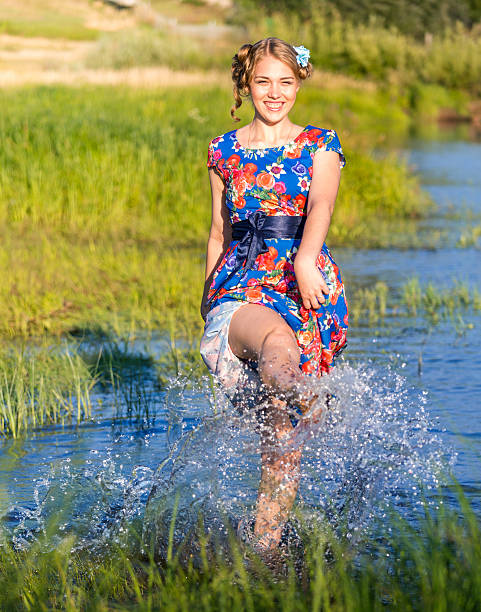 Beautiful blonde girl having fun kicking water in river
