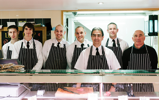 Seven butchers stand behind the counter at a family-run butcher's shop, Frampton's Butchers, Bridport, Dorset. 