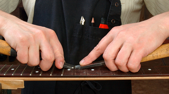 Luthier establishes frets in a signature stamp of an electric guitar, replacement of frets on new.