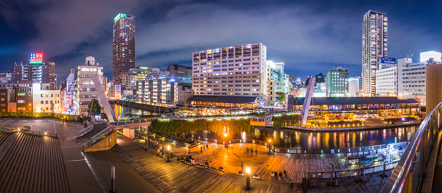 Panoramic view across the Dotonbori canal to the waterside promenade, highrise apartment buildings, restaurants and office blocks in the heart of downtown Osaka, Japan. ProPhoto RGB profile for maximum color fidelity and gamut.