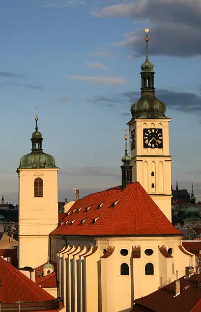 The spire and clock tower of the Church of St.James located close to the Old Town Square is bathed in warm morning sun light. 