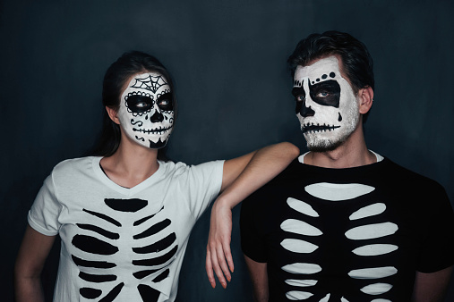 Loving couple with skull face art in costume of skeletons on dark background, Halloween theme