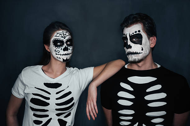 Couple in costume of skeletons Loving couple with skull face art in costume of skeletons on dark background, Halloween theme face paint halloween adult men stock pictures, royalty-free photos & images