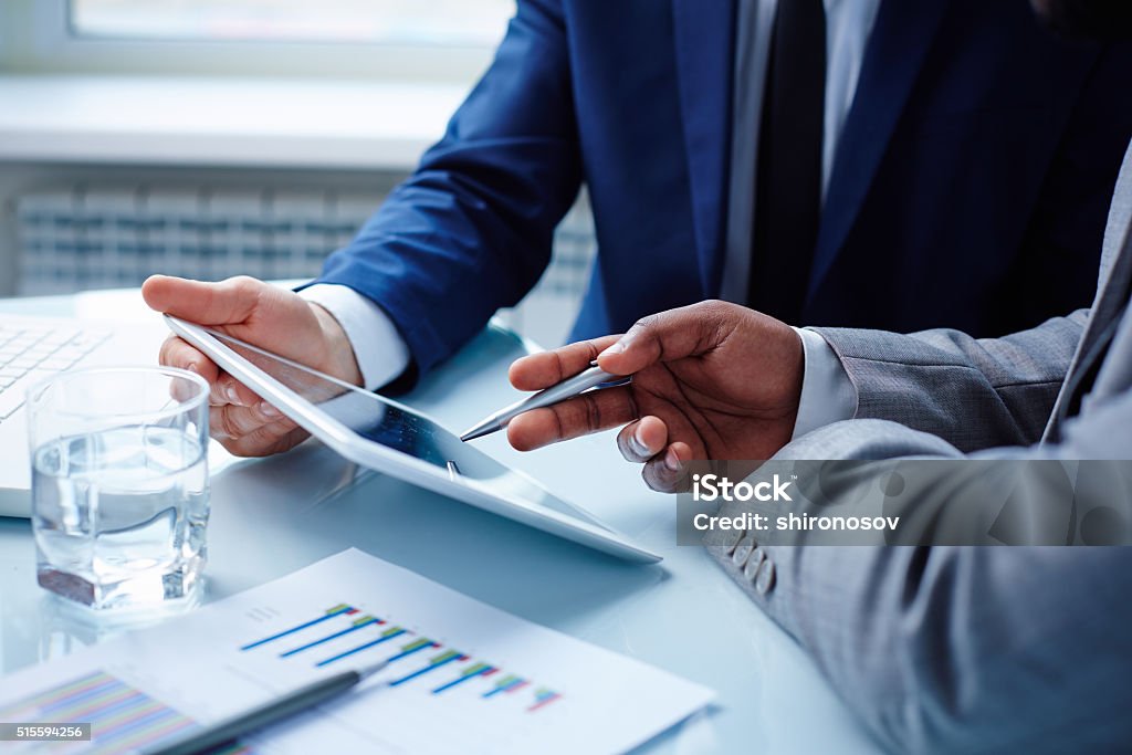 Pointing at touchpad Image of businessmen discussing data in touchpad at meeting Digital Tablet Stock Photo