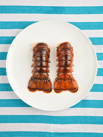 Two lobster tails on plate top view on striped texture