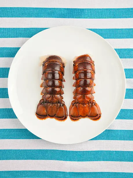 Two lobster tails on plate top view on striped texture