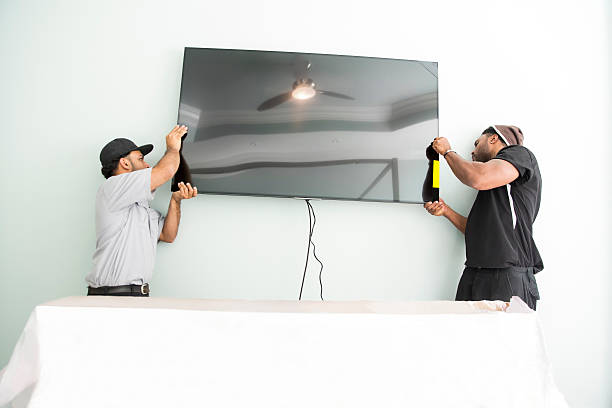 Series-Real televison installers hanging large flat screen TV on wall Two real television installers are hanging a large flat screen TV on a white wall in a home. They have mounted a bracket on the wall to hold the TV.  This is a real situation with real people. There are connecting brackets on the TV.  Taken with Canon 5D Mark3. installing tv stock pictures, royalty-free photos & images