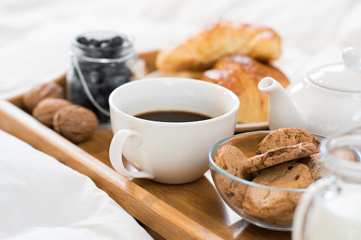Breakfast in bed with hot coffee and croissants. Healthy breakfast kept on bed. Close up of a cup of tea with cookies on wooden tray in bed.
