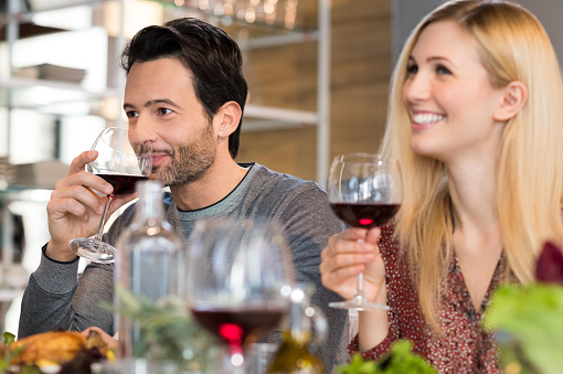 Portrait of a young couple hosts. Young couple enjoying wine and drinks with friend. Couple enjoying lunch at home. Happy friends eating together at home.