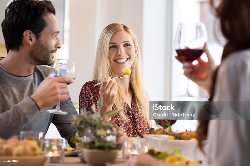 Friends eating together Happy young friends enjoying lunch at a restaurant. Woman eating baked potatoes while friends drinking red wine. Happy smiling friends having dinner at home. Restaurant Stock Photo