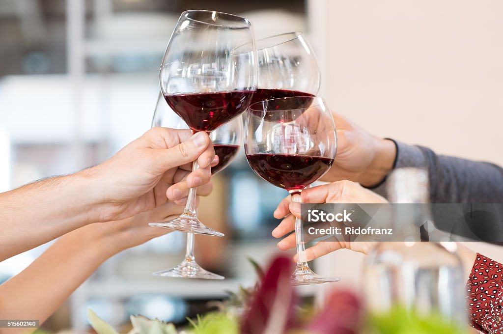 Toasting glasses Close up of glasses raising a toast at lunch. Closeup of friends toasting glasses of red wine in a party. Group of friends a toast to the cheers of red wine at restaurant. Celebratory Toast Stock Photo