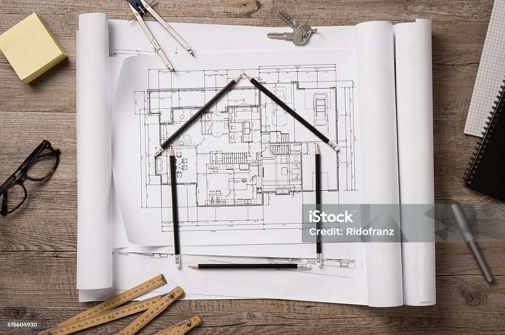 New home project Top view of architectural blueprints, rolls and drawing instruments on the worktable. Shape of house with black pencils on a project house. Architectural drawings with house keys on wooden table, new home concept. House Stock Photo