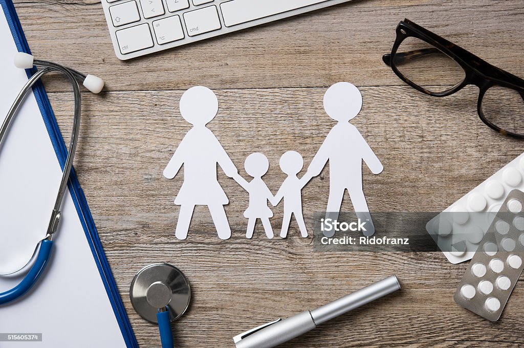 Family healthcare Top view of family paper chain on a doctor desk. Medical worktable with keyboard, blue stethoscope, pills and eyeglasses. Family healthcare, medicine and insurance concept. Pediatrician Stock Photo