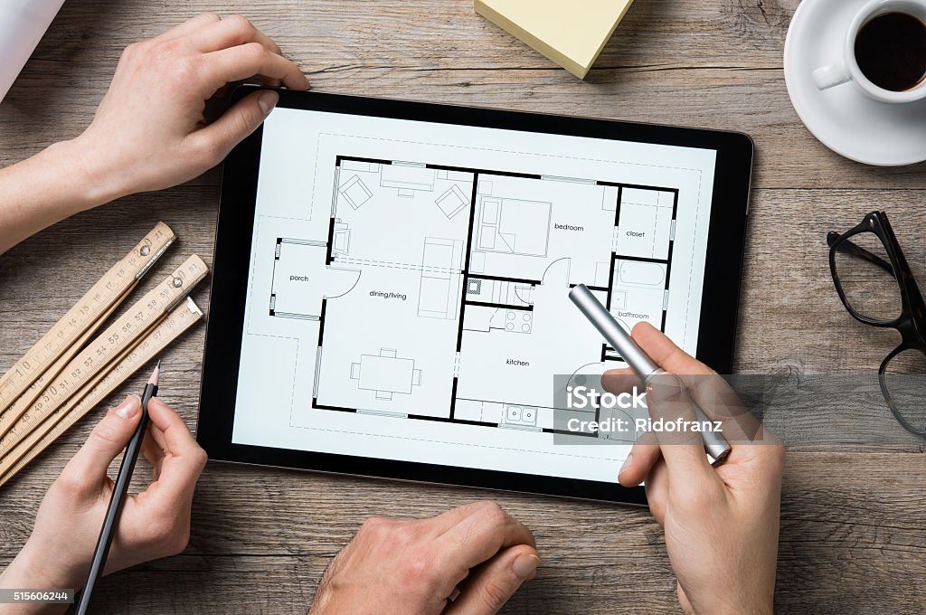 Architect working on digital tablet Team of architects working on the house project on a wooden table. Top view of hands pointing architectural project on digital tablet. Interior designer hand working with digital tablet. Interior Designer Stock Photo