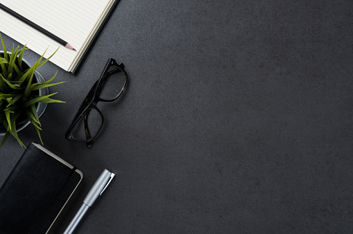 High angle view of businessman desk with organizer, pen, glasses and green plant. Top view of office supplies on blackboard background with copy space.